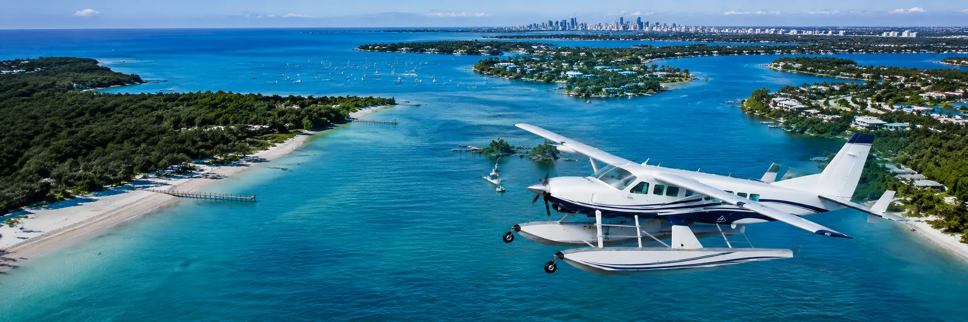 A seaplane on floats over a sheltered bay with the Miami skyline far off on the horizon