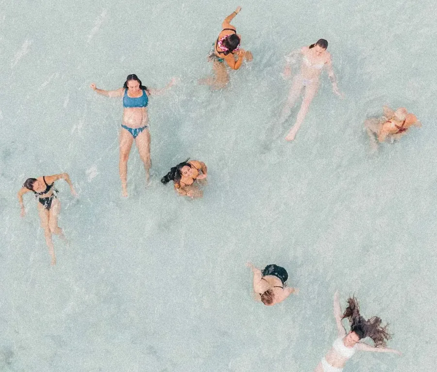 A group of friends standing and floating in shallow clear turquoise water, seen from directly above