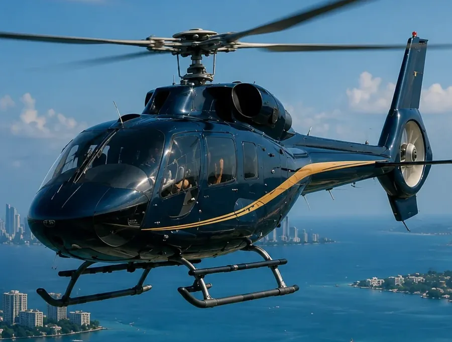 A dark blue and gold helicopter in flight over Biscayne Bay, rotor and tail in full view, the Miami skyline on the water behind it