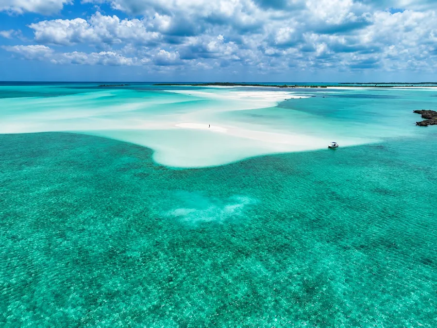 A white sandbar curving through turquoise shallows off Man-O-War Cay from the air, a small boat pulled up at its edge