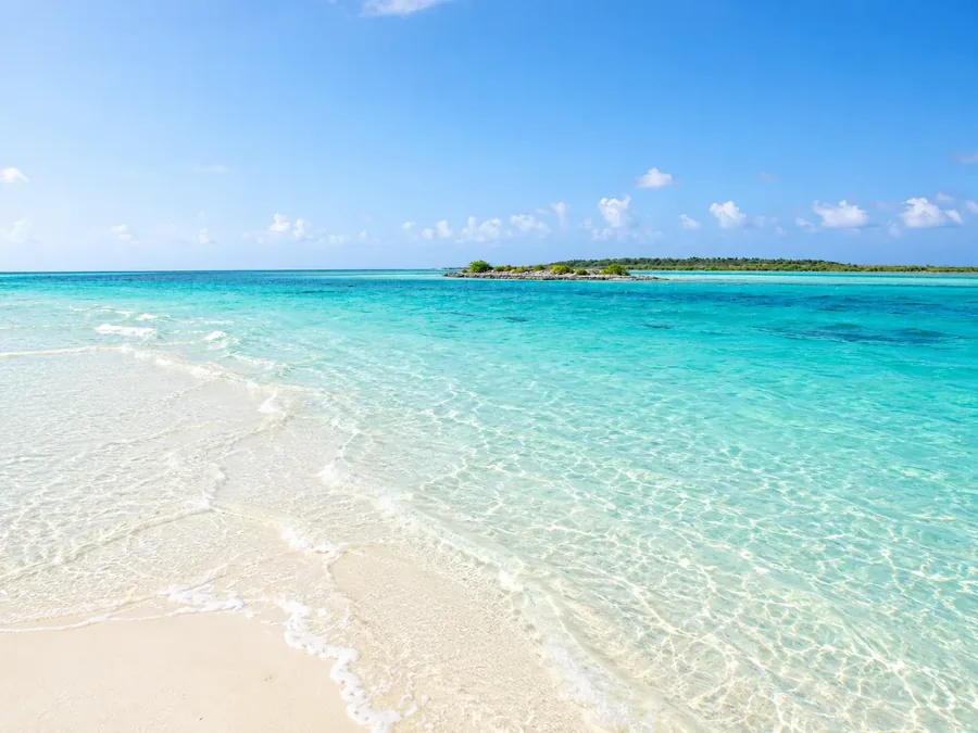 Clear turquoise shallows running over pale sand to a low green cay on the horizon at Mayaguana