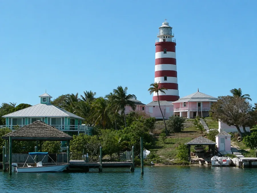 The candy-striped Hope Town lighthouse on Elbow Cay above pastel cottages and a boat dock on the water