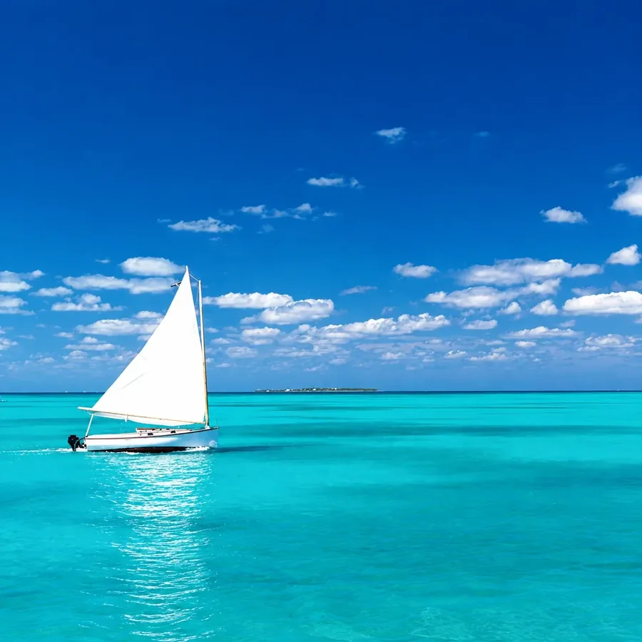 A small sailing dinghy on flat turquoise water with a low cay on the horizon