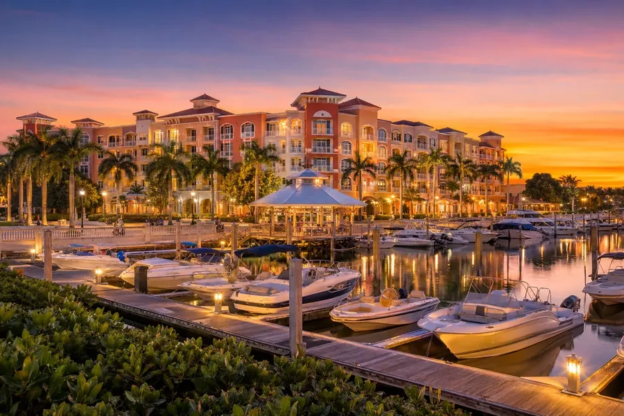 The Naples waterfront at sunset, boats along the docks in front of lit waterside buildings and palms