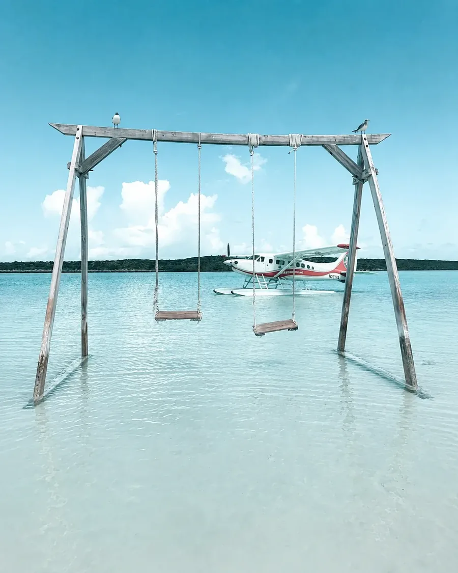 A swing set standing in ankle deep water with a seaplane on floats waiting behind it