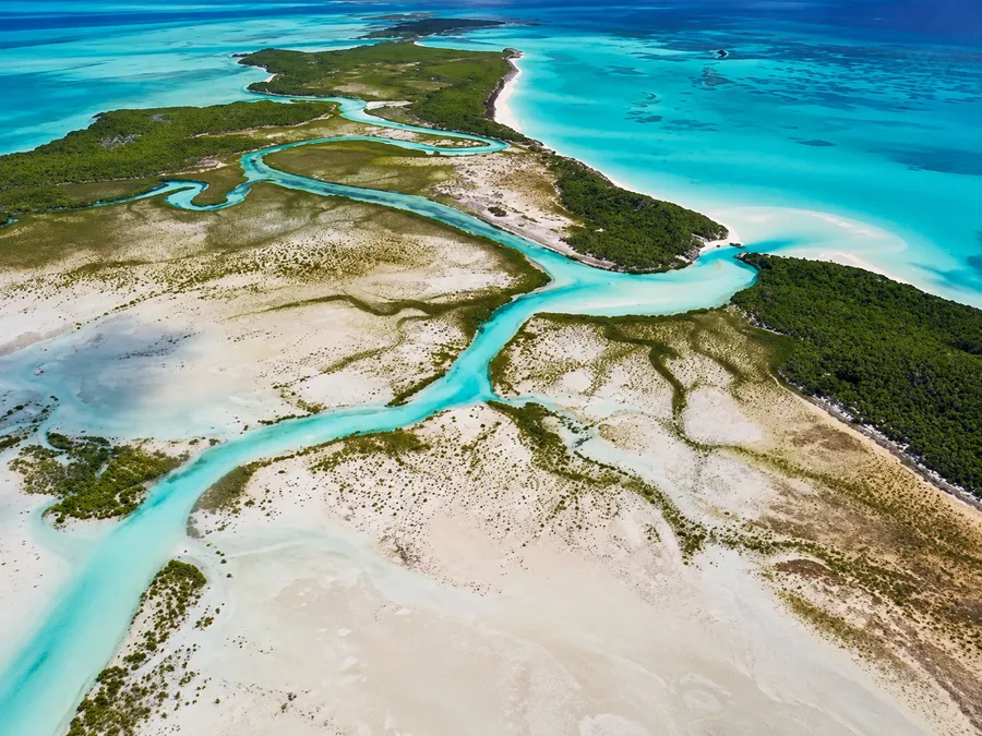 A turquoise creek winding through mangroves and white tidal flats on Shroud Cay in the Exumas, seen from the air