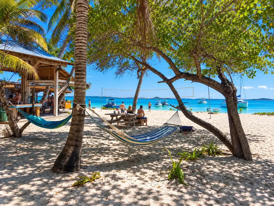 Hammocks strung between palms on white sand beside a beach bar on Stocking Island, boats anchored in the turquoise harbour off Great Exuma